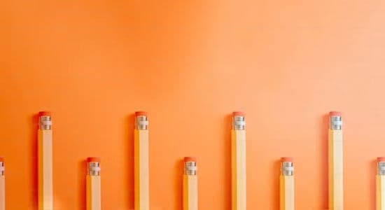 A row of pencils of different lengths, arranged in ascending order on an orange background.