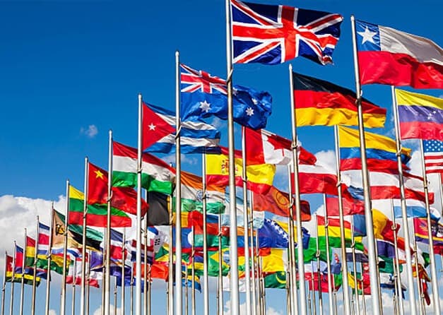 A row of flags representing various countries from around the world, waving in the wind.